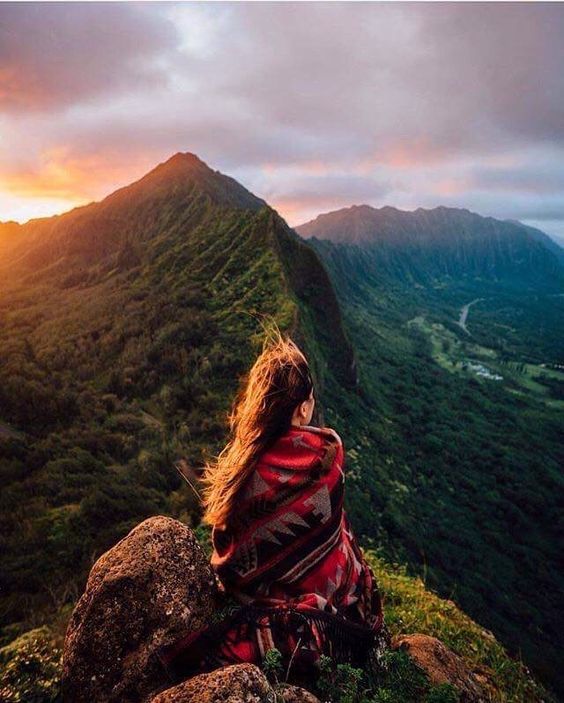 Zdjęcie w poście przedstawia: Zamyślona kobieta siedząca na szczycie góry patrząca na dolinę