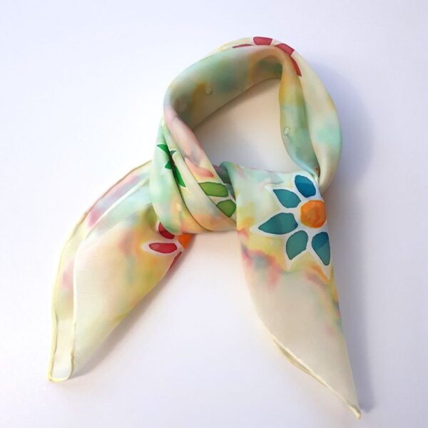 Zdjęcie poglądowe zawiązanej ręcznie malowanej apaszki jedwabnej z motywami kwiatów w kolorach niebieskich, zielonych i czerwonych na jasnocytrynowym tle z tęczowymi barwami z efektem akwareli.